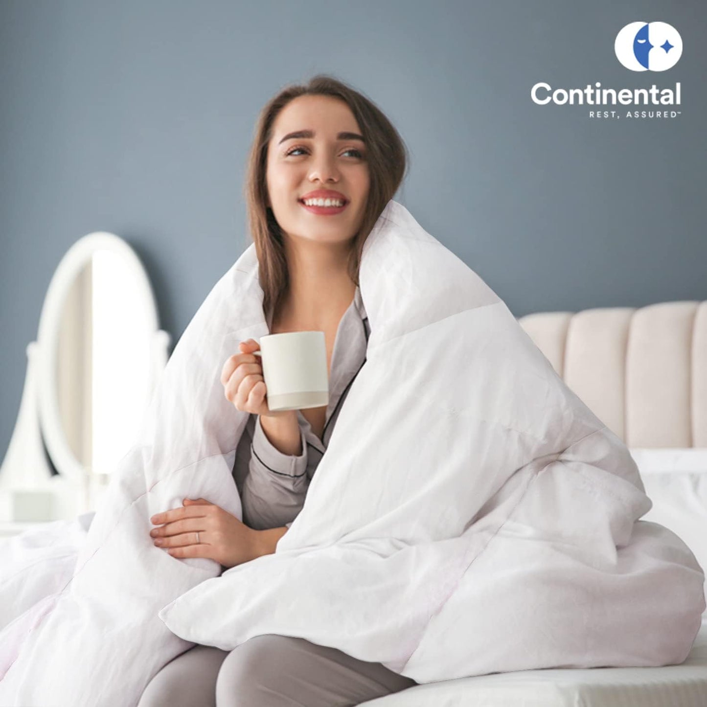 A smiling woman wrapped in a luxurious white duvet, enjoying a warm drink in a cozy bedroom. The Continental Bedding logo is displayed in the corner, emphasizing warmth and comfort.