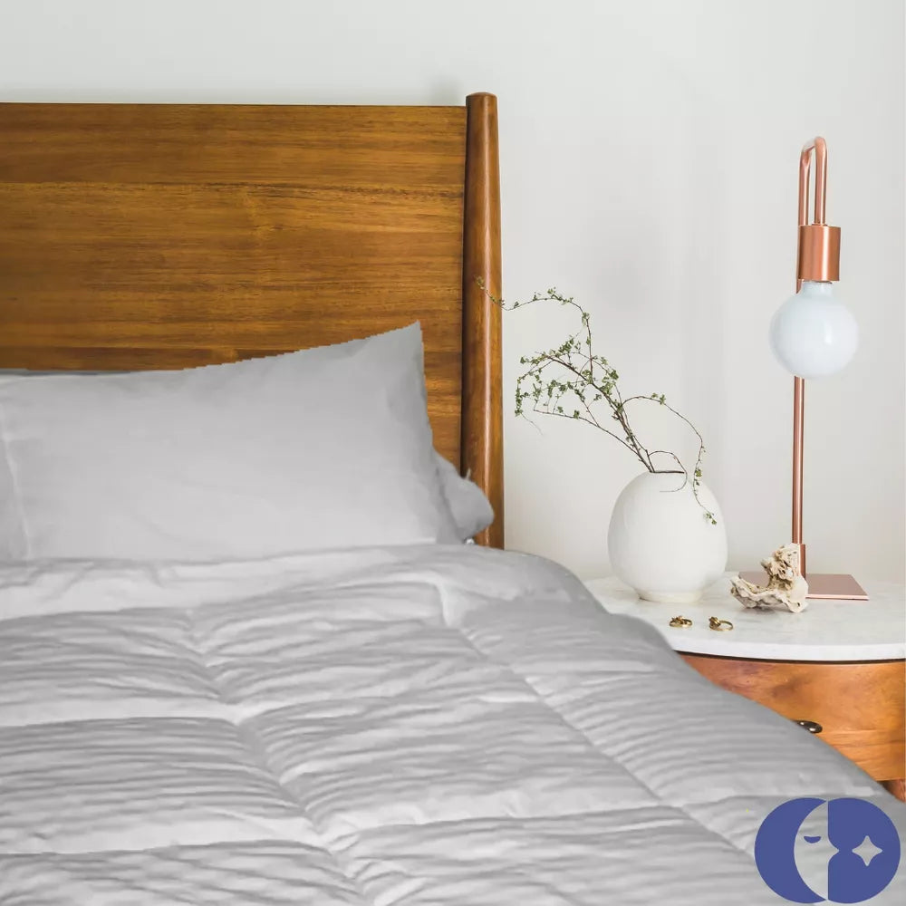 A neatly made bed featuring a plush white duvet in a bright bedroom with elegant curtains, showcasing its soft texture and high-quality craftsmanship.