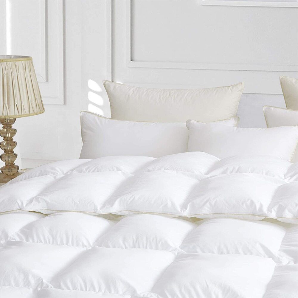 A close-up of a plush white duvet with baffle box construction, resting on a bed with matching pillows in a bright, elegant bedroom, highlighting its softness and loft.