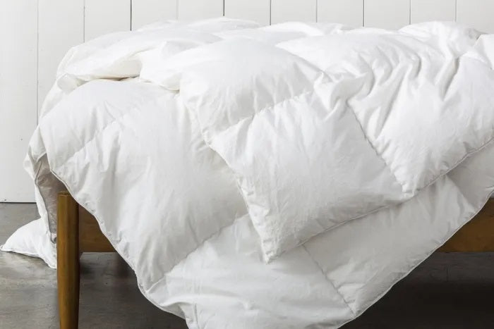 A fluffy white duvet draped over a wooden bed, styled in a rustic yet modern bedroom setting, emphasizing its premium loft and warmth.