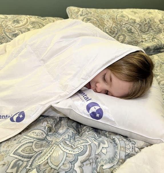 A young child sleeping peacefully on a Continental Bedding toddler goose down pillow, wrapped in a cozy white comforter. The pillow and blanket feature the Continental Bedding logo, emphasizing softness and luxury.