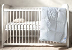 A luxurious white Continental Bedding toddler goose down duvet insert draped over a modern white crib in a minimalist nursery. The baffle-box construction and premium loft create a cozy and inviting sleep environment, perfect for little ones.
