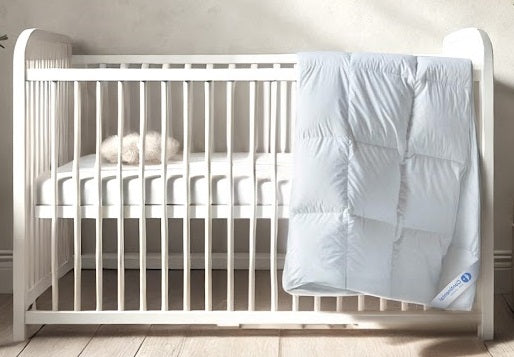 A luxurious white Continental Bedding toddler goose down duvet insert draped over a modern white crib in a minimalist nursery. The baffle-box construction and premium loft create a cozy and inviting sleep environment, perfect for little ones.
